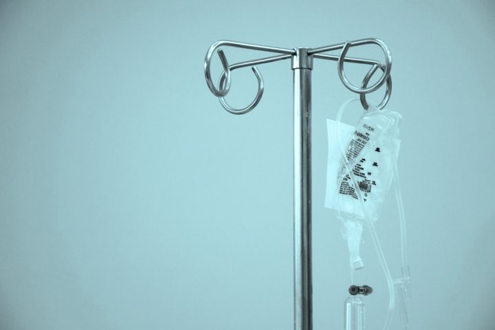 A close-up of a metal IV pole holding a plastic bag of intravenous fluid in a hospital setting.