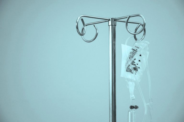 A close-up of a metal IV pole holding a plastic bag of intravenous fluid in a hospital setting.