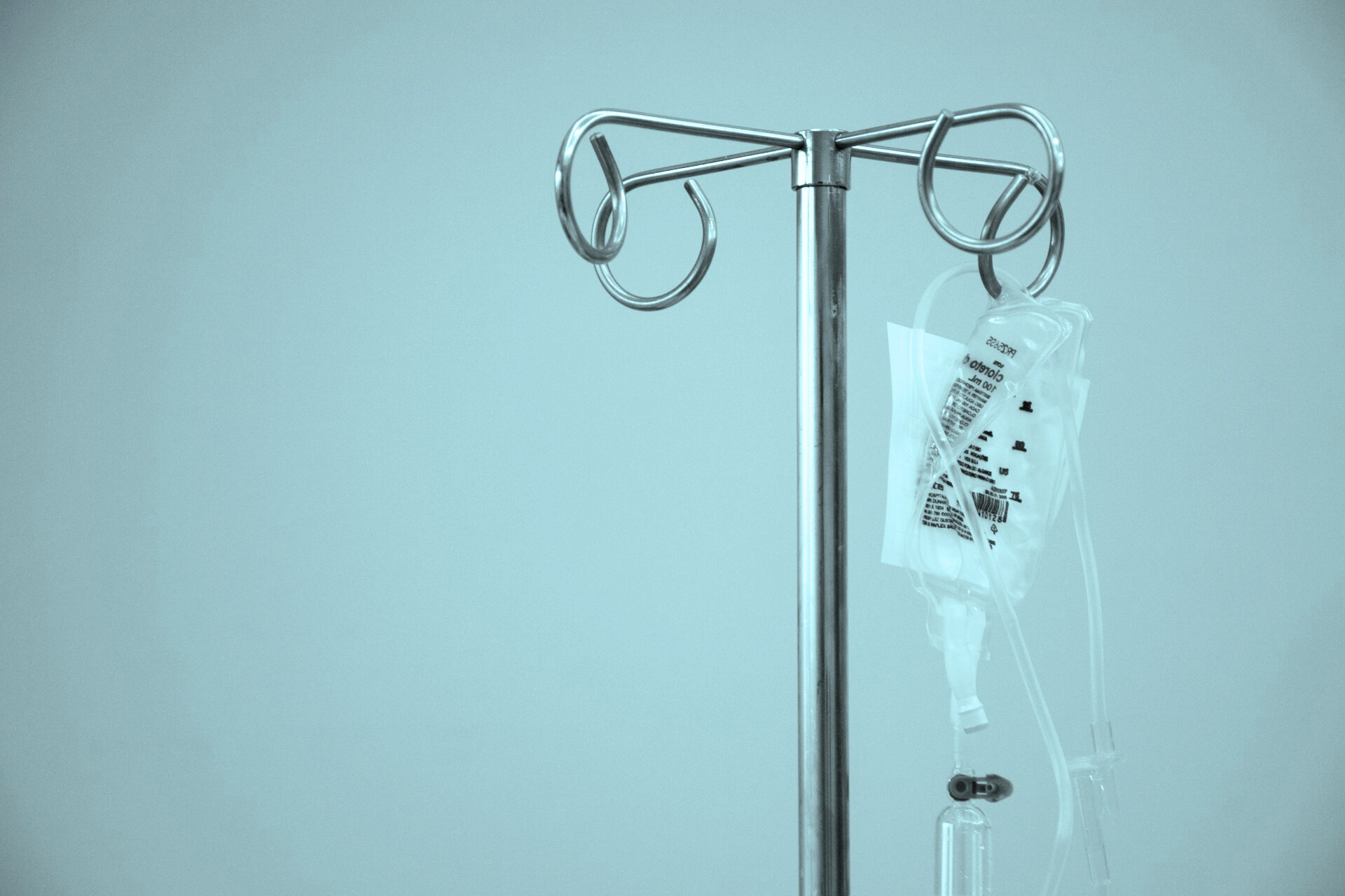 A close-up of a metal IV pole holding a plastic bag of intravenous fluid in a sterile setting.